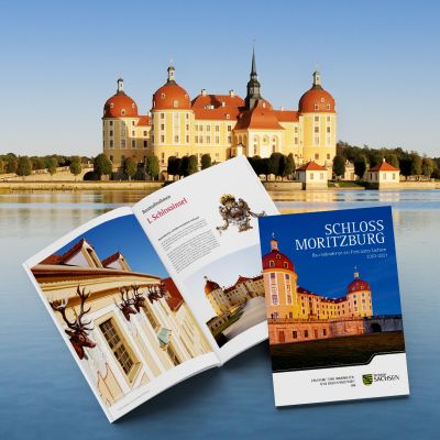 Aufgeschlagen Seiten und Cover der Broschüre „Schloss Moritzburg – Baumaßnahmen des Freistaates Sachsen 2003–2021“ montiert vor einem Bild des Schlosses