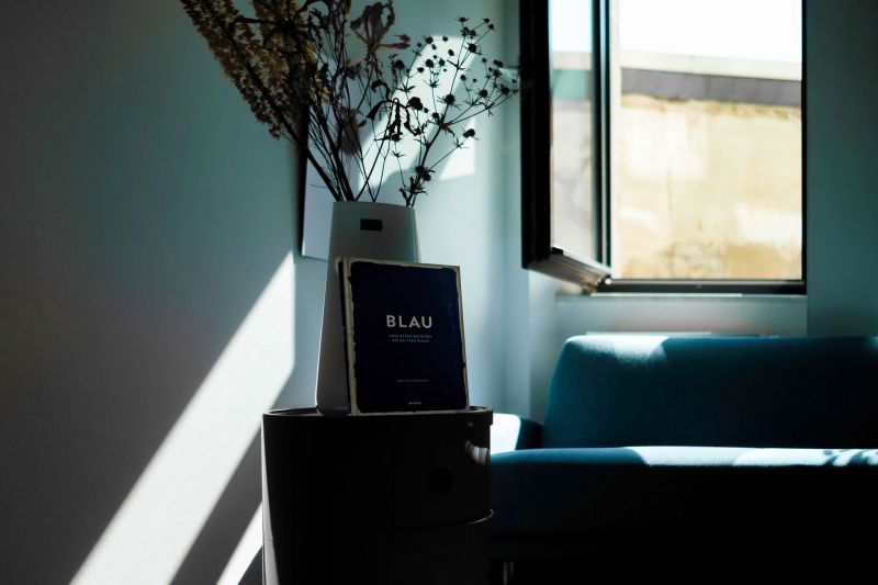 Detailaufnahme in den Räumen der Agentur zeigt eine Vase an der eine Broschüre lehnt, im Hintergrund ist ein blaues Sofa zu sehen und ein Fenster ist geöffnet